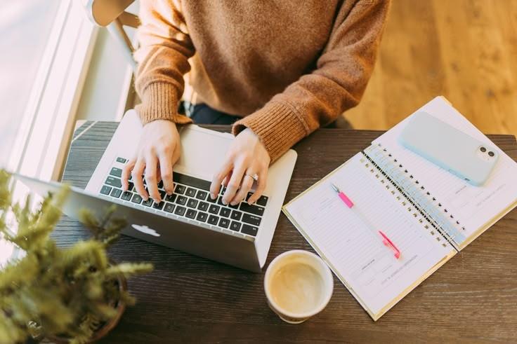 A person working beside an open planner and a cup of coffee