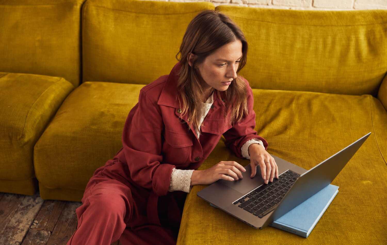 A woman working on a laptop on a yellow sofa